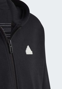 Czarna bluza z kapturem na zamek, o miękkiej fakturze, z białym logo w trzy paski na klatce piersiowej i pasiastą podszewką.