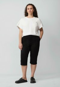 Witte t-shirt met korte mouwen met een klein kleurrijk geborduurd ontwerp, gecombineerd met aansluitende zwarte cropped pants en zwarte instapschoenen.