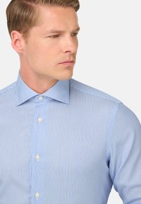 Gaiši zils pogājams krekls ar smalkām baltām svītrām, izklāta apkakle un standarta pogas. Audumam ir gluda tekstūra.