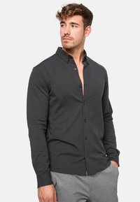 Camisa abotonada de un gris oscuro con un ligero brillo, que cuenta con un collar clásico y mangas largas, hecha de una tela suave y ligera.