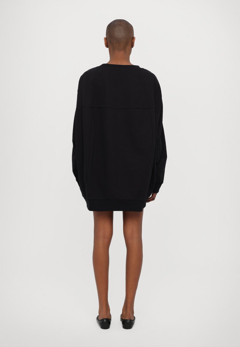 Sweatshirt noir surdimensionné avec des manches longues, un col rond et une couture dans le dos. Texture de tissu lisse et douce.