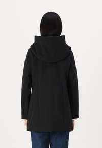 Manteau noir avec une grande capuche, présentant un design sur mesure et des coutures structurées. Le matériau semble lisse ; la vue de dos montre des lignes simples et sans embellissements.