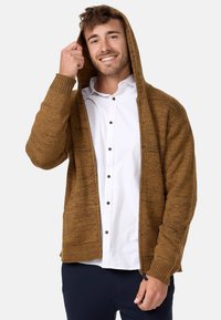 Brown knitted hoodie with a textured pattern, front zipper, ribbed cuffs, and open front, worn over a white button-up shirt.