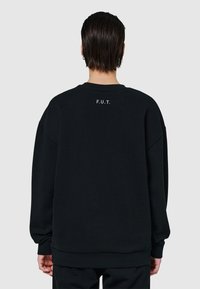 Svart sweatshirt med rund hals, oversized passform och "F.U.T." tryckt i vitt på baksidan. Har långa ärmar och ribbade fickor.