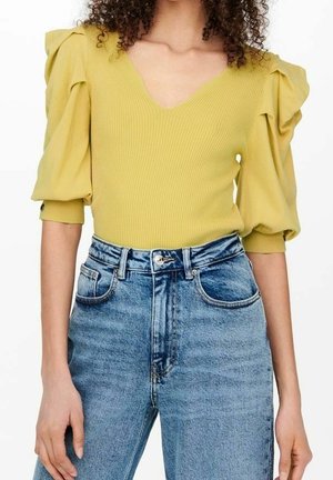 Woman wearing a yellow ribbed V-neck top with puffed sleeves and high-waisted light blue denim jeans.