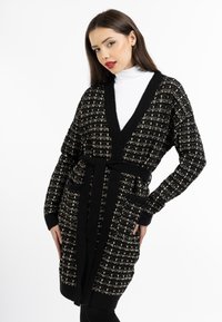 Cardigan lavorato a maglia nero e oro con scollo a V, maniche lunghe, due tasche e cintura da annodare in vita. Motivo testurizzato su tutta la superficie.