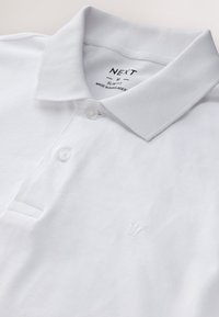 Weißes Slim-Fit-Poloshirt mit Kragen, zwei Knöpfen und kleinem, gesticktem Kronenlogo auf der Brust.