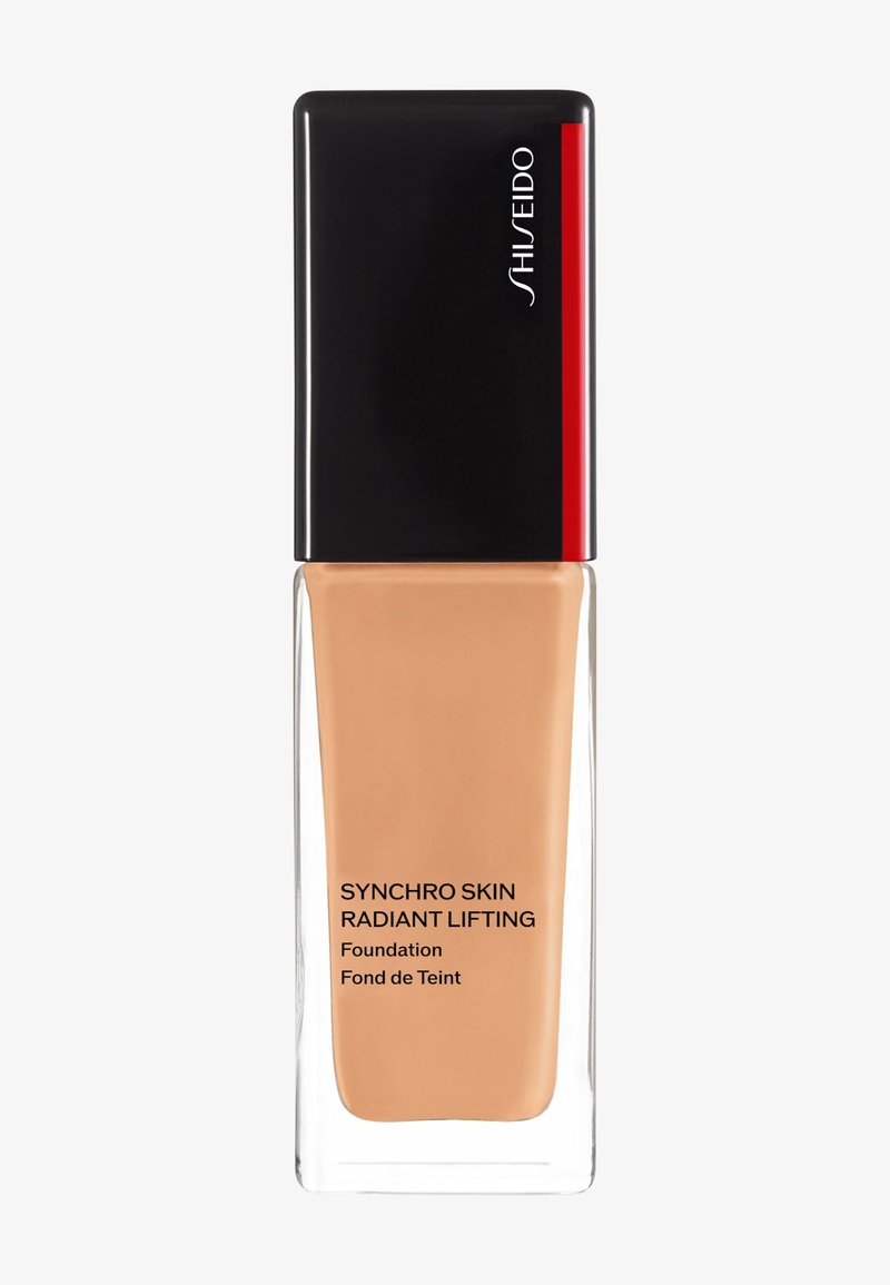 Shiseido Synchro Skin Radiant Lifting foundation i en klar glassflaske med svart lokk. Produktetikett i svart tekst på lys beige bakgrunn.