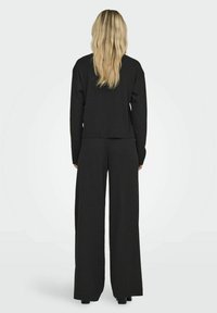 Schwarzes geripptes Zweiteiler-Outfit mit einem croppenden Oberteil und weit geschnittenen Hosen, beide aus einem strukturierten Stoff und in entspannter Passform.
