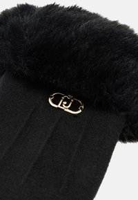 Accessorio nero con una parte superiore in pelliccia sintetica morbida e una base nera liscia. Presenta un dettaglio di chiusura color oro nella parte anteriore, che arricchisce il suo design.