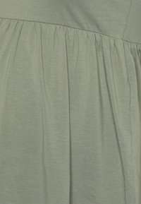 Měkká zelená tkanina s nařaseným švem, který vytváří záhyby a strukturu, ukazující detailní vzor textilie a šití.