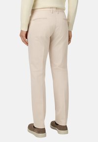 Pantalones beige claros de algodón, con un corte recto, dos bolsillos traseros y combinados con zapatos de tacón oscuros.