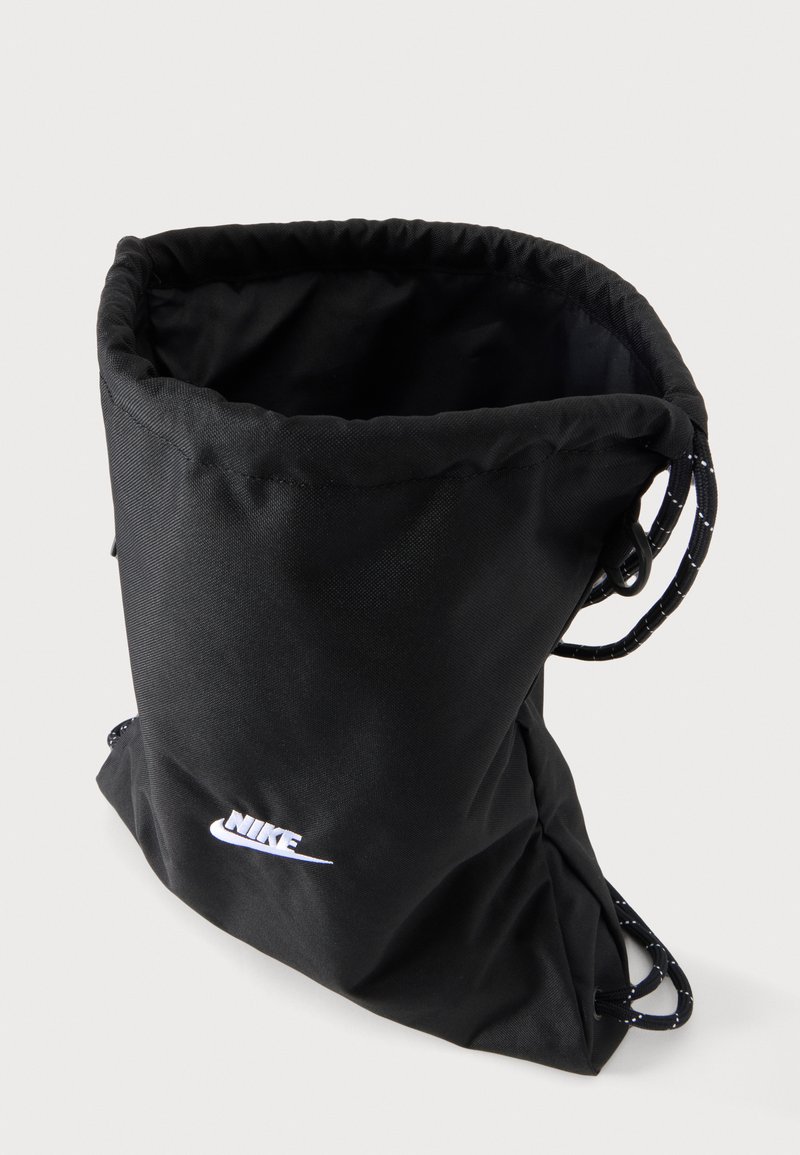 Black Nike drawstring gym bag with white logo and cinch cords on a light background.