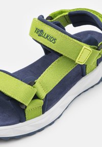 Barnsandaler med gröna nylonremmar, marinblå vadderad innersula och vit gummisula. Har justerbar spänne för passform.