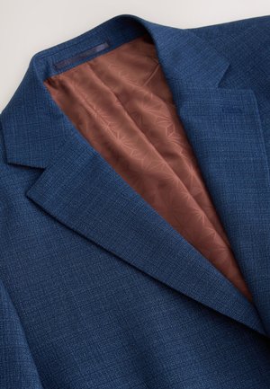 Veste bleu marine avec un extérieur texturé, dotée d'une doublure intérieure marron avec un motif géométrique. Notable col cranté et coupe ajustée.