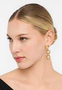 Orecchini a forma di cuore in tono dorato con tre cuori collegati e finitura lucida. Il design pende elegantemente da un perno.