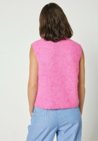 Roosa ilma varrukateteta kudum, millel on tekstureeritud pind, �ümmargune kaelus ja pehme, karvane kangas. Kombineeritud siniste triibuliste pükstega.