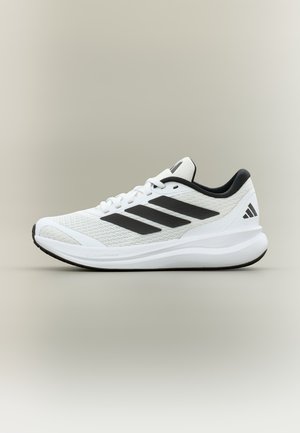 Chaussure de course Adidas blanche et noire avec trois bandes noires sur le côté et semelle amortissante sur un fond neutre.