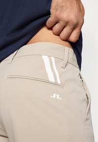 Μπεζ παντελόνι με υφή, με λευκές ρίγες στην πίσω τσέπη, διαθέτει μία μόνο πίσω τσέπη και λογότυπο από πάνω.