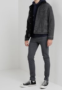 Black denim jacket with a dark blue hoodie underneath, grey skinny jeans, and black high-top sneakers with white soles.