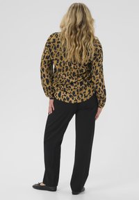 Haut à imprimé léopard brun et noir avec manches longues, associé à un pantalon large noir et des chaussures plates noires, vu de derrière.