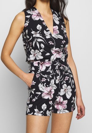 Czarny kombinezon w kwiaty z głębokim dekoltem w serek, bez rękawów i wiązany w talii. Na miękkim materiale wzór białych i różowych kwiatów.