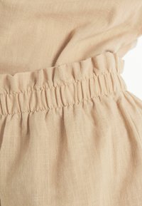 Tessuto beige chiaro con una finitura morbida e testurizzata. Il capo presenta una vita elastica e tessuto arricciato per una vestibilità rilassata.