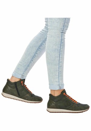 Des baskets montantes vertes avec des lacets orange et une fermeture éclair, présentant des sections perforées et une tige texturée, reposant sur une semelle légère et à motifs.