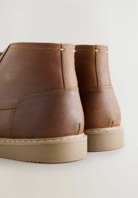 Brązowe skórzane buty z gładką teksturą, z przeszyciami, okrągłym noskiem i jasną gumową podeszwą.