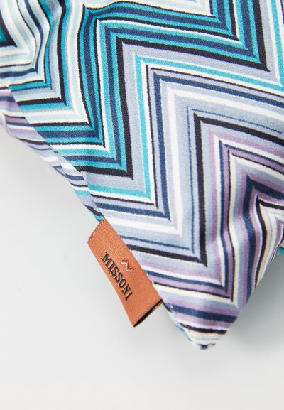 Textilný vankúš so vzorom v zubatých líniách v odtieňoch modrej, fialovej a čiernej. Obsahuje hnedú koženú nálepku označenú "MISSONI."