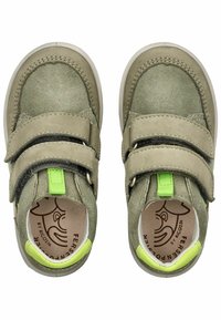 Zelené semišové boty se dvěma pásky na suchý zip a jasně zeleným akcentem. Interiér ukazuje světlou hnědou vložku s logem. Kulatý design špičky.