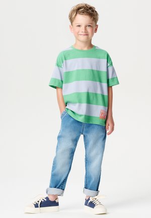 Grün und grau gestreiftes kurzärmeliges T-Shirt, blaue Jeans mit hochgerollten Ärmeln und marineblaue Sneaker mit beigen Akzenten. Lässiges Outfit für Kinder.