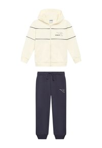 Felpa con cappuccio crema con zip e strisce nere, caratterizzata da un logo; abbinata a pantaloni della tuta blu navy con logo bianco. Entrambi realizzati in tessuto morbido.