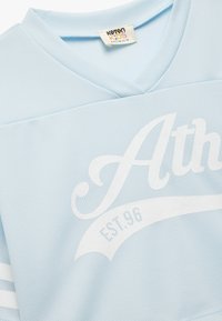 Lysblå trøje lavet af struktureret stof, med et hvidt "Ath" grafik og "EST.96" detalje. V-hals design med korte ærmer.