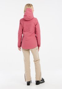 Wasserabweisende rosa Jacke mit Kapuze, elastischen Bündchen und geformtem Saum. Kombiniert mit hellbeigen Hosen mit Reißverschlusstaschen und ausgestellten Beinen.