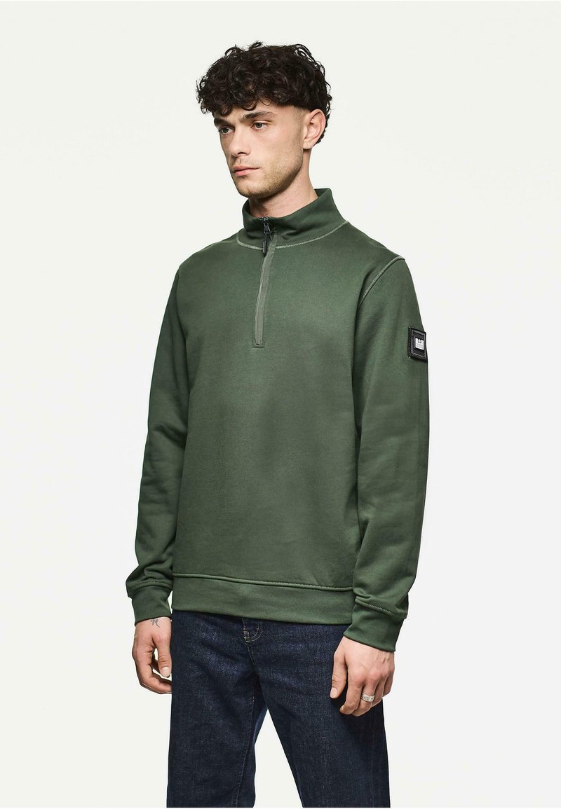 Oliwkowa bluza z długim rękawem z zamkiem na szyi, z ribbowanymi mankietami, o gładkiej fakturze i małą naszywką z logiem na lewym rękawie.