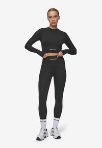 Fekete bordás, hosszú ujjú crop top és magasan derekú leggings szett, fehér "PEGADOR" felirattal és sima, sportos fazonban. Fehér sportcipők.