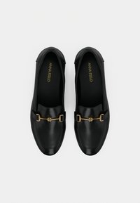 Mocassins en cuir noir avec une texture lisse, un bout arrondi et des accents de ferrures dorées sur le devant. Le branding est visible à l'intérieur.