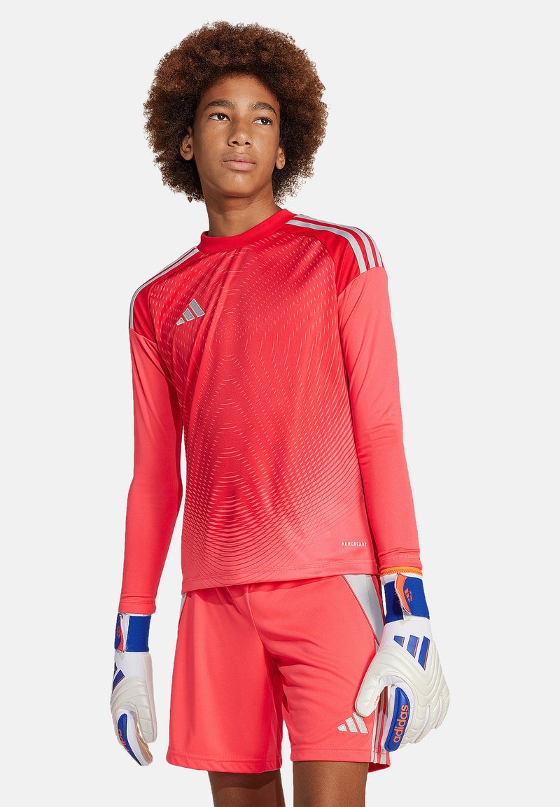 Rote sportliche Torwartuniform mit langen Ärmeln, die ein Farbverlauf-Design aufweist. Begleitet von weißen Handschuhen mit blauen und roten Akzenten.