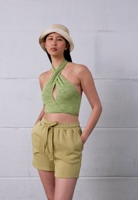 Top verde sem mangas com design cruzado, combinado com calções leves de oliva com elástico na cintura e cordão. Visual descontraído.