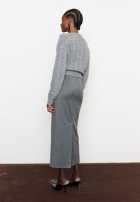 Hallitatud hall kampsun, millel on kaablipattern, koos istuva halli seelikuga, millel on külgslit, kantud mustade kõrgete kontsadega kingadega.