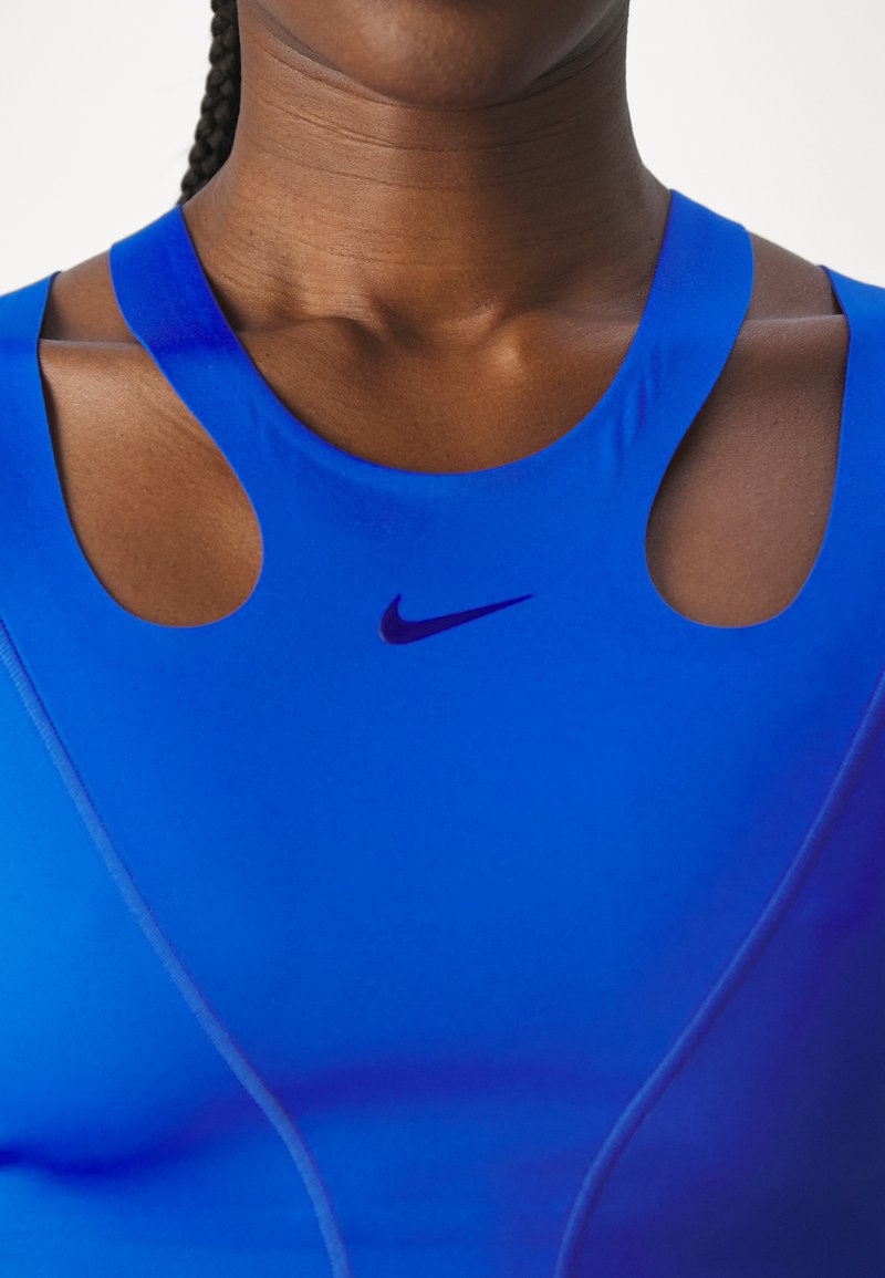 Gros plan sur une personne portant un haut de sport Nike bleu vif avec des découpes aux épaules et des cheveux tressés visibles à l'arrière.