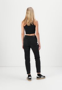 Svarta högmidjade jeans med smal benfack, tillsammans med en svart crop top och svarta och vita sneakers. Slät tyg med minimal hårdvara.