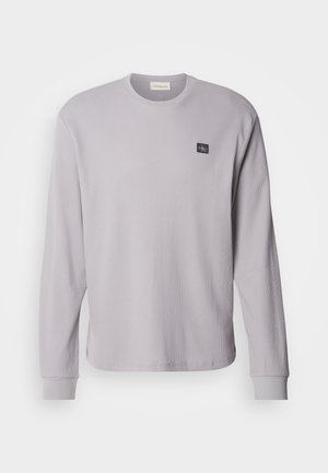 Lange mouwen grijze wafelgebreide shirt met een ronde halslijn en geribbelde manchetten; bevat een klein zwart logopatch op de linkerborst.