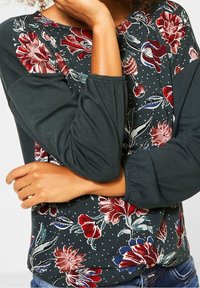 Floral long-sleeve top featuring a dark green body, patterned red and blue flowers, and gathered sleeves, made from soft cotton material.