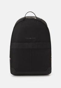 Zaino nero con una finitura in tessuto liscia, design arrotondato, manico superiore e dettagli del logo discreti. Include schienale imbottito e spallacci regolabili.