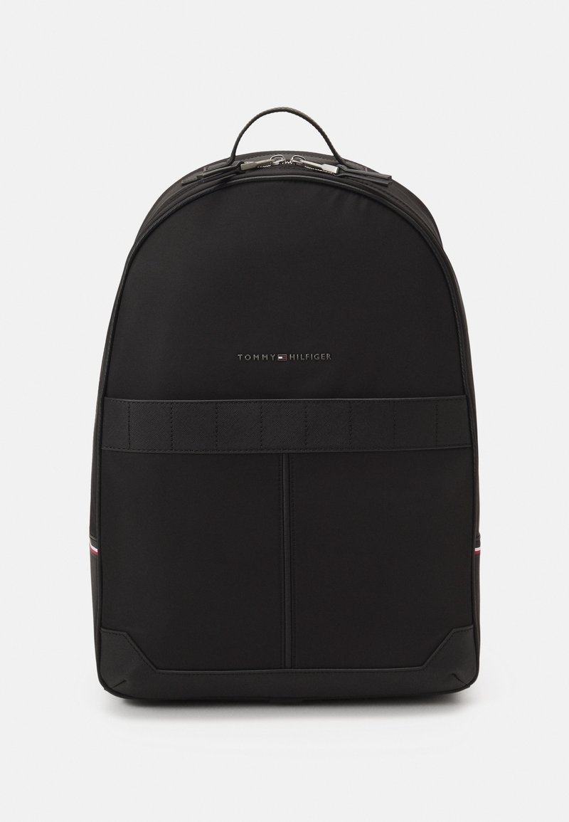 Zaino nero con una finitura in tessuto liscia, design arrotondato, manico superiore e dettagli del logo discreti. Include schienale imbottito e spallacci regolabili.