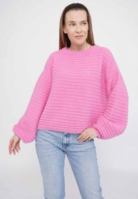 Rosa gestreifter Pullover mit weiten Ärmeln und Rundhalsausschnitt, kombiniert mit hellblauen Jeans. Weicher Stoff, lässiges Design.