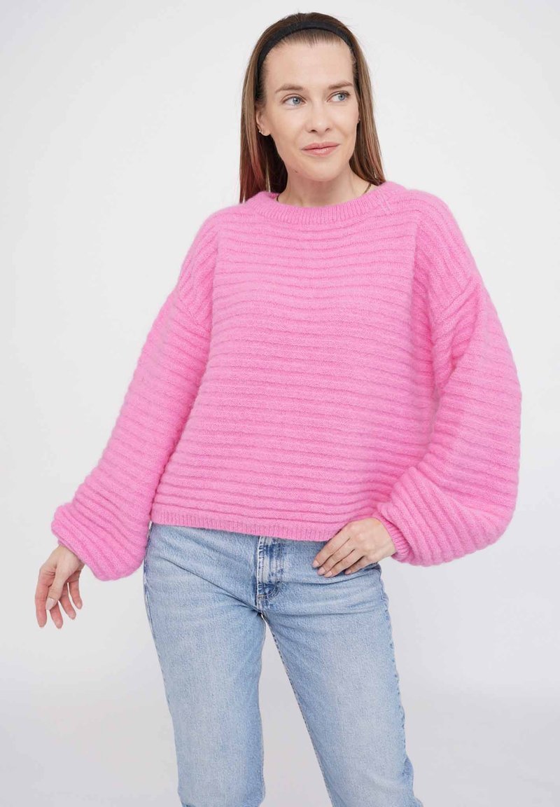 Rosa gestreifter Pullover mit weiten Ärmeln und Rundhalsausschnitt, kombiniert mit hellblauen Jeans. Weicher Stoff, lässiges Design.