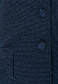 Navy blue textured fabric with a close-up view of two buttons and a side pocket. The material appears woven and durable.